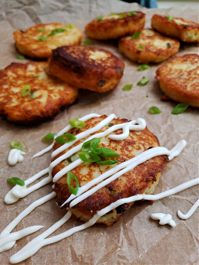 mashed potato patties made from leftover mashed potatoes on a parchment lined serving plate drizzled with sour cream and garnished with scallions