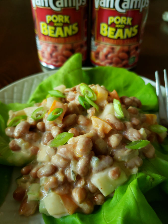 Best pork n beans salad recipe on a white plate with lettuce and canned pork and beans in the background