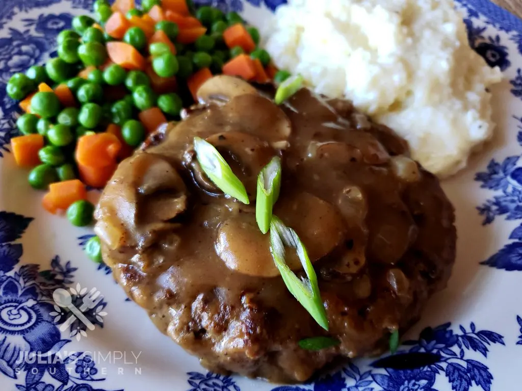 Southern Salisbury Steak Recipe with mushroom gravy served with a side of mashed potatoes and peas and carrots