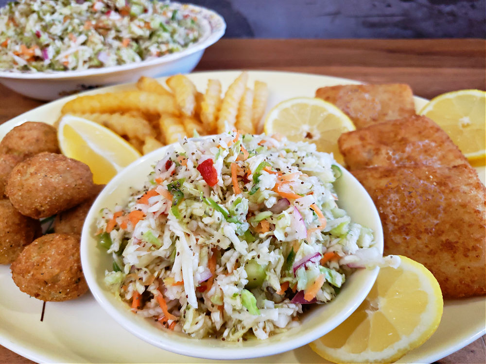 Vinegar coleslaw served on a platter with lemon garnishes, fish, french fries, and hushpuppies