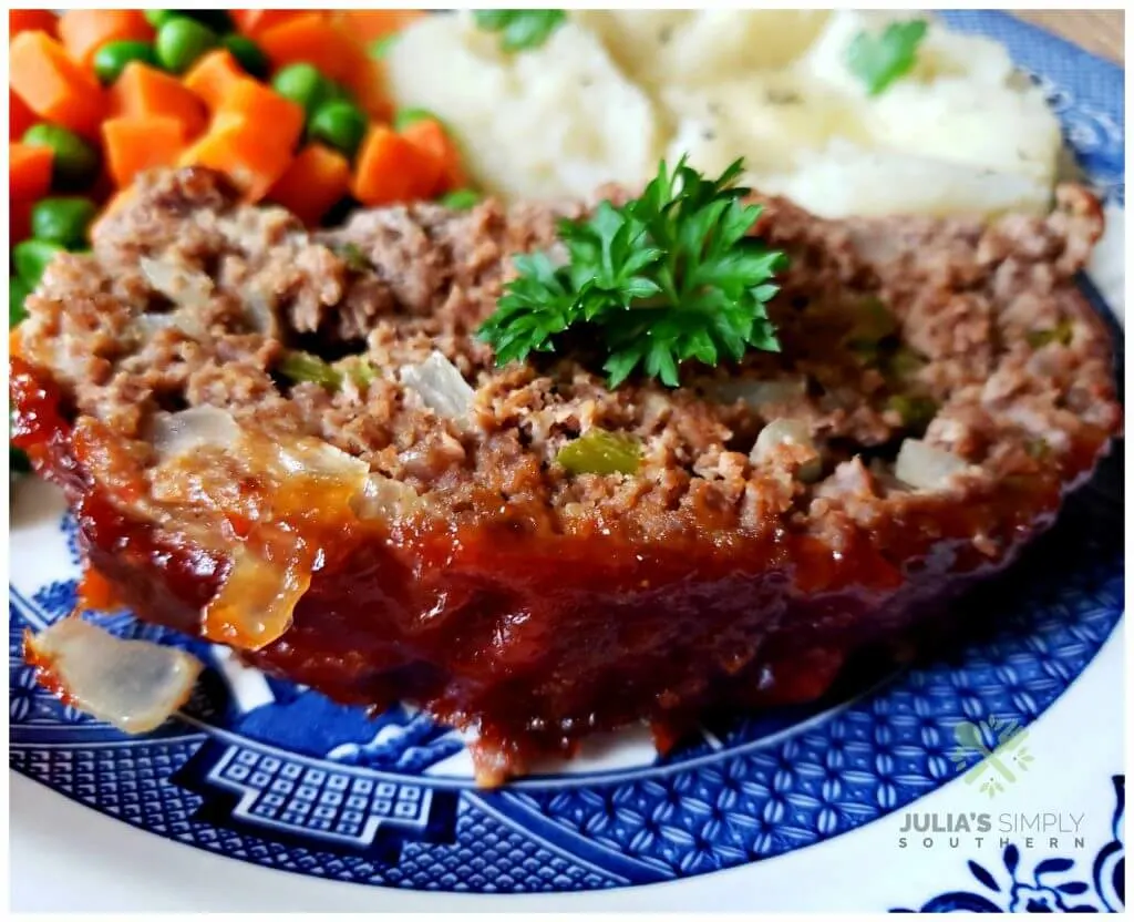 Delicious slice of Southern Style Meatloaf served with mashed potatoes and peas and carrots with a parsley garnish