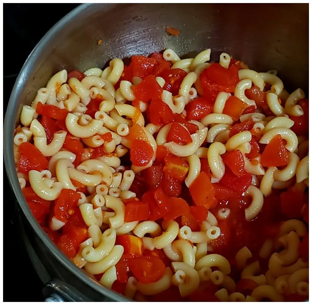Macaroni pasta and diced tomatoes combined in a silver pot