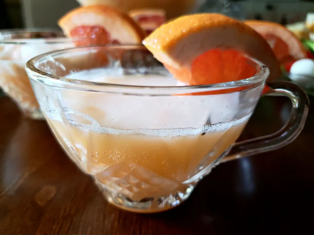 Glass of easy party punch garnished with a wedge of fresh sliced orange