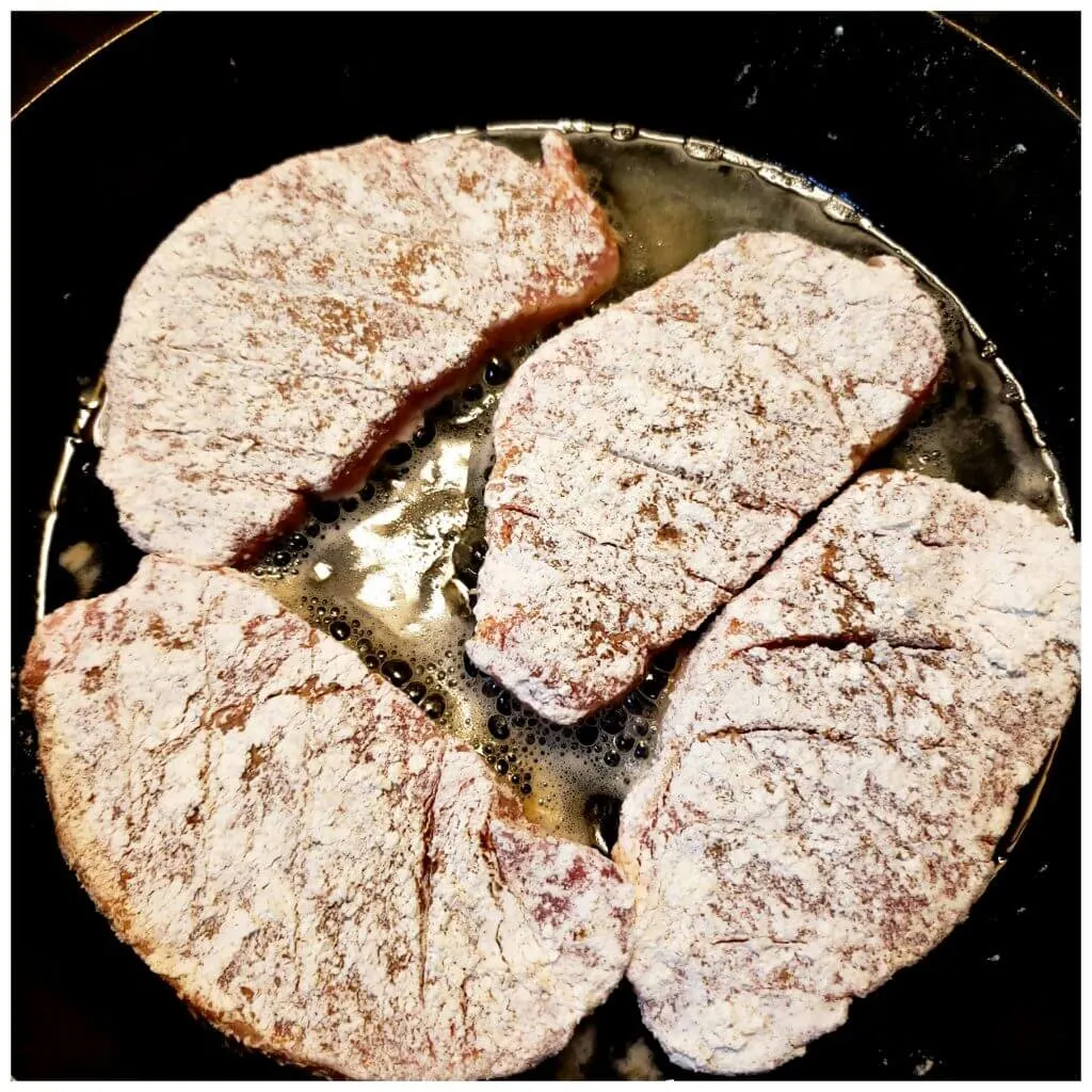 Pork chops seasoned and dredged in flour browning in cooking oil in a cast iron skillet