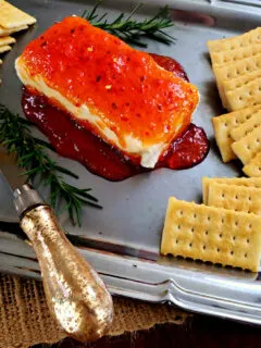 Best pepper jelly cream cheese appetizer on a silver serving platter with crackers garnished with rosemary sprigs