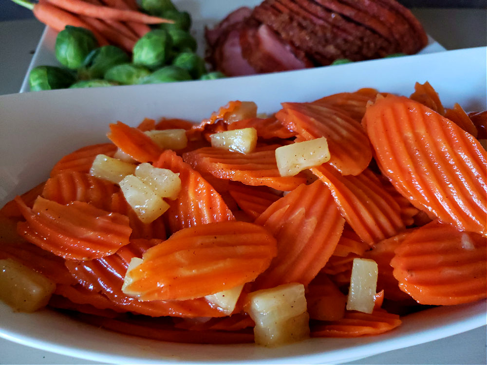 Carrots and pineapple side dish. glazed ham with carrots and brussels sprouts in background.