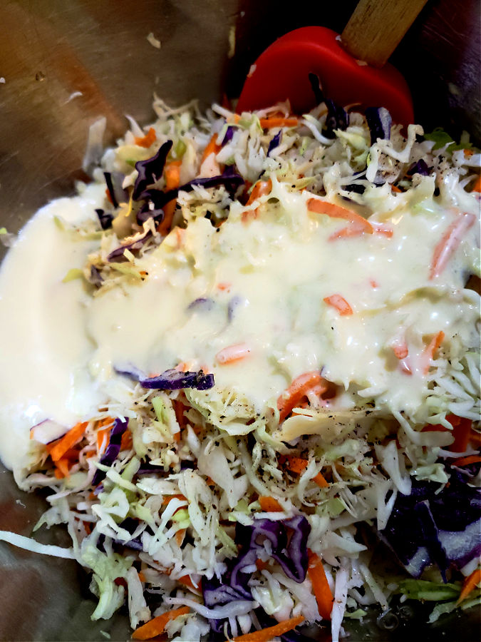 Creamy dressing for slaw in a mixing bowl with shredded cabbage salad mix