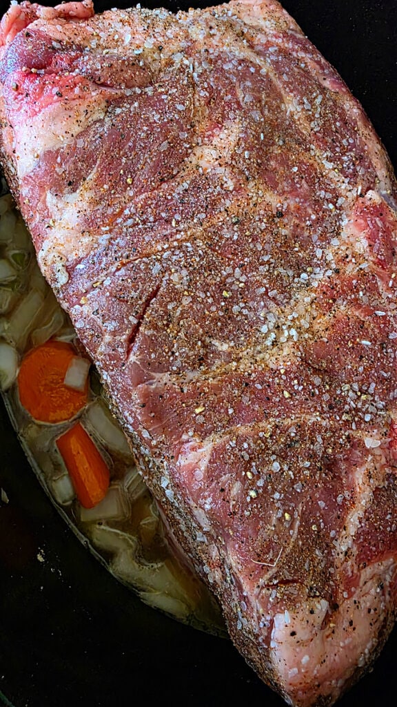 Placing seasoned pork shoulder on bed of vegetables in crockery of slow cooker