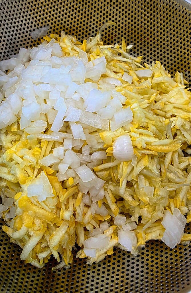 grated squash and diced onion in a colander draining excess water