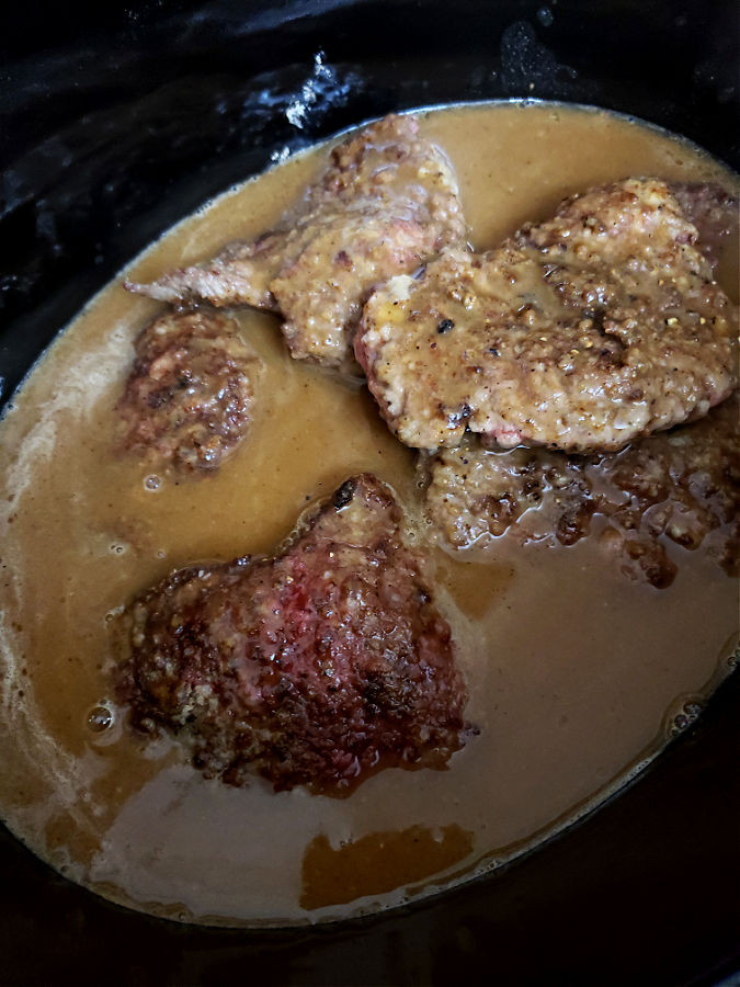Adding the gravy mixture to the crockery with cube steaks before slow cooking until tender