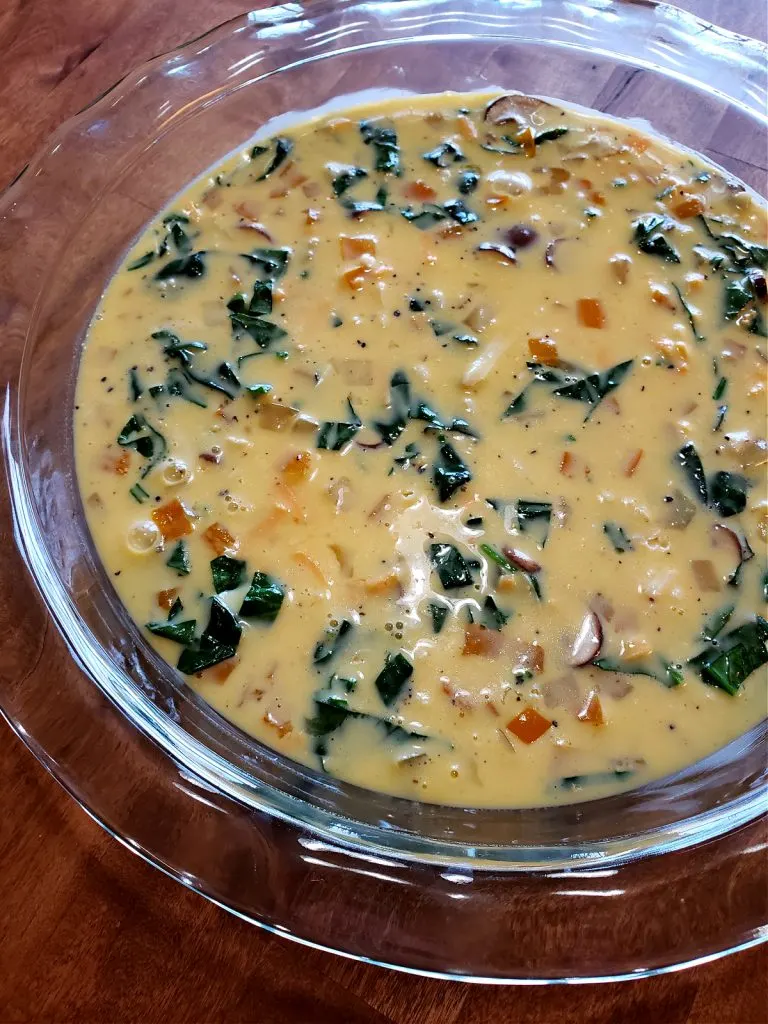 Glass pie dish with quiche mixture ready for the oven