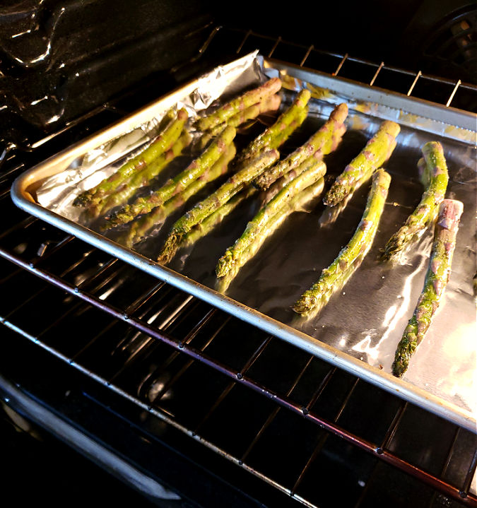 Sheet pan with thick asparagus spears in the oven for roasting