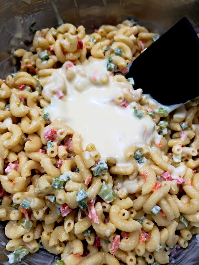 adding the reserved mac salad dressing to the macaroni salad to refresh it.