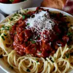 Spaghetti Sauce Recipe on a bed of fresh cooked pasta topped with grated Parmesan cheese and garnished with fresh parsley