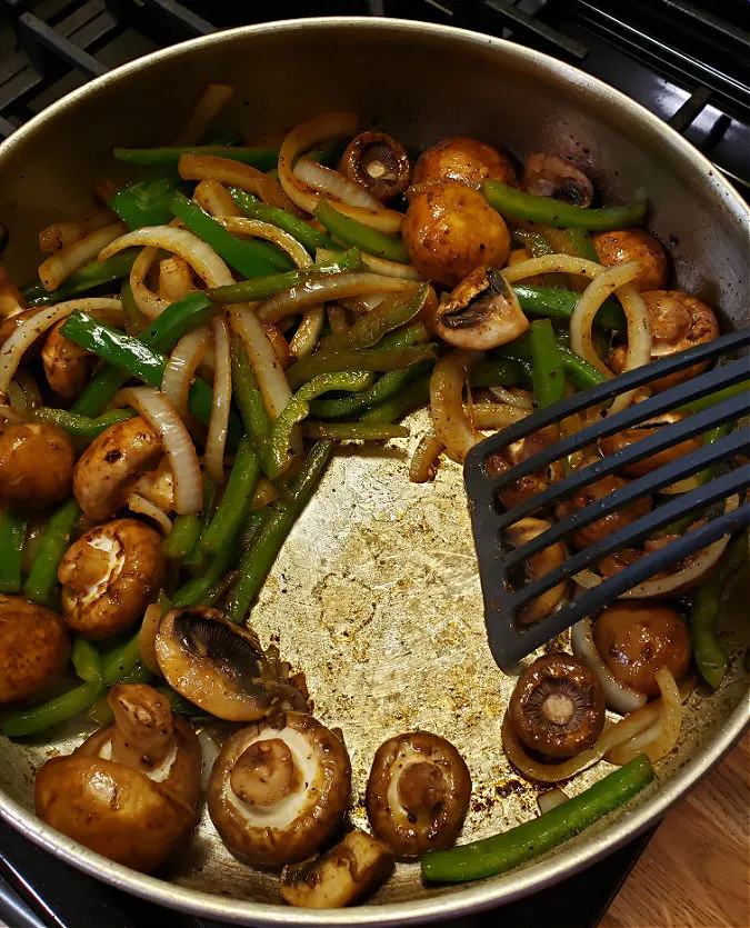 skillet sautéing onions, peppers and baby bella mushrooms to deglaze the pan