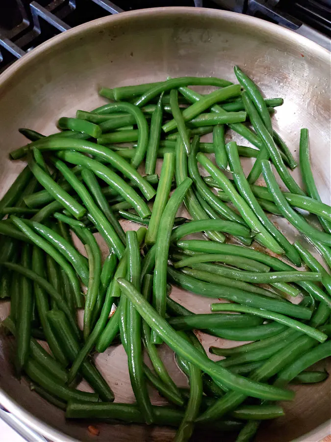 Blanched fresh green beans in a skillet with bacon fat for sautéing.