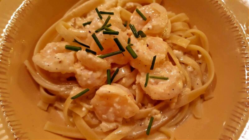 shrimp with garlic cream sauce over pasta and garnished with chives