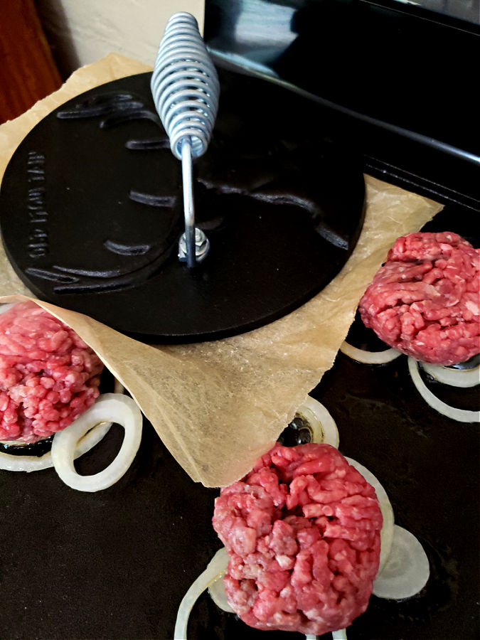 Using a cast iron press to smash a burger patty on a hot griddle