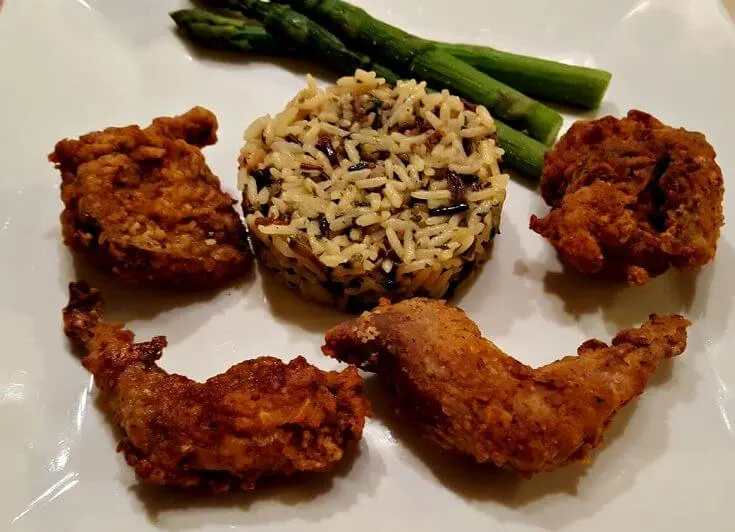 fried quail on a plate with wild rice and asparagus