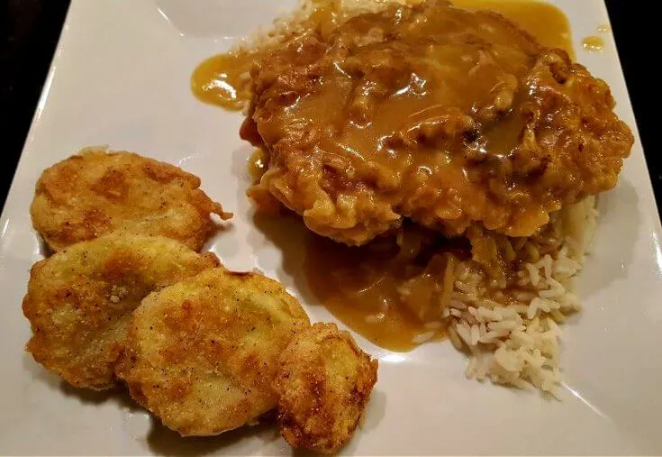 Smothered Pork Chops on a white plate with rice and fried yellow squash
