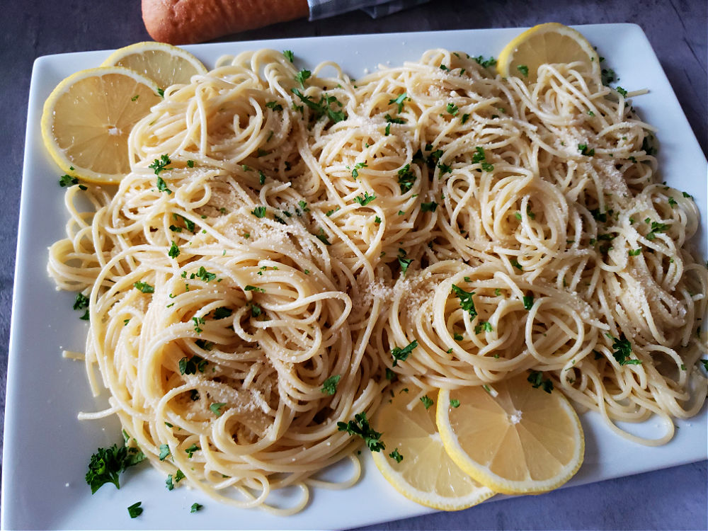 Spaghetti with infused olive oil sauce with lemon wedge garnish and fresh parsley with grated Parmesan Cheese
