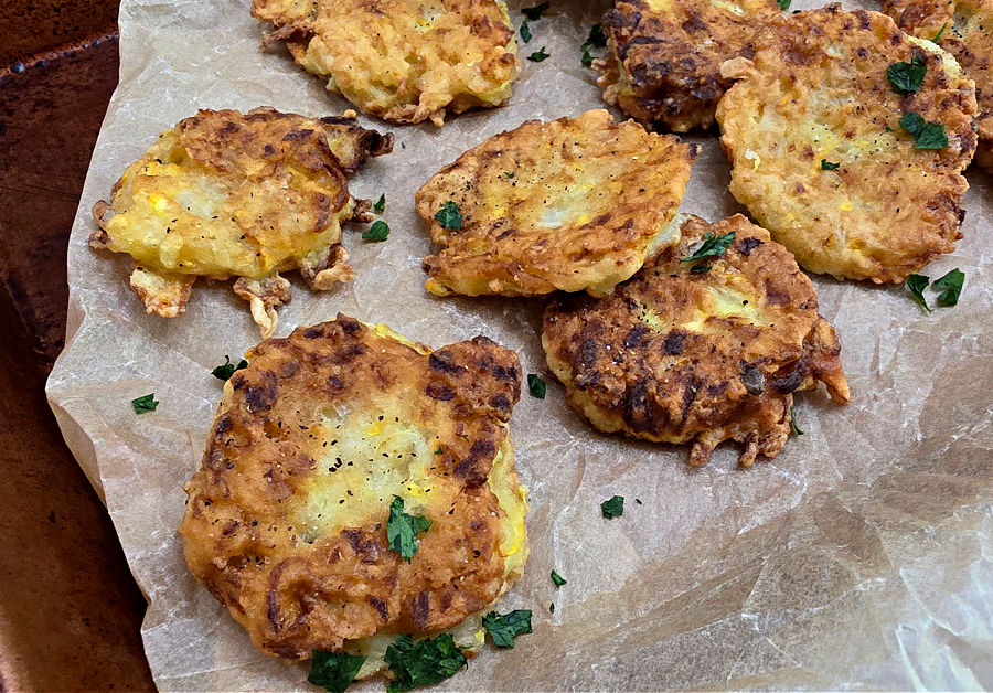 Golden brown and crispy yellow squash fritters on a baking sheet garnished with a sprinkle of parsley