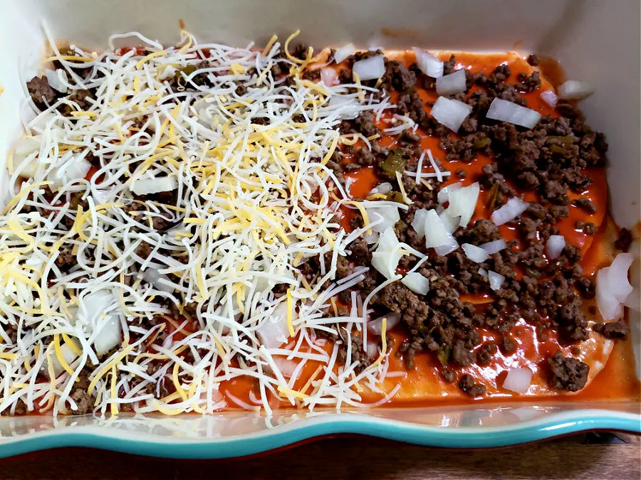 Layering tortillas, ground beef, onions and cheese into a casserole dish