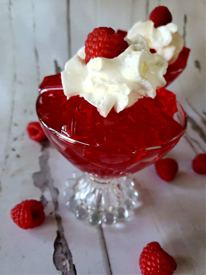 Sugar Free Raspberry Jell-O in a dessert glass topped with whipped cream and fresh raspberries