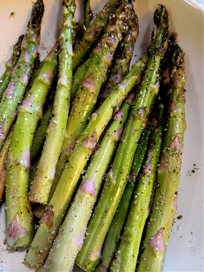 adding olive oil to asparagus and seasoning before roasting
