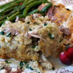 beautiful holiday plate of food with moist cornbread dressing sauteed green beans and roasted turkey with cranberry garnish and giblet gravy