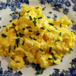 fluffy scrambled eggs on a blue and white plate garnished with chopped fresh chives