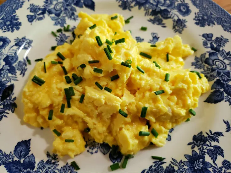 fluffy scrambled eggs on a blue and white plate garnished with chopped fresh chives