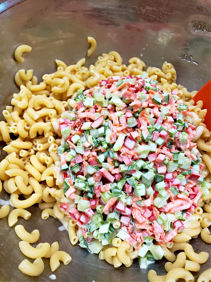 adding the creamy dressing with sweet vegetables to cooked elbow pasta to mix for macaroni salad