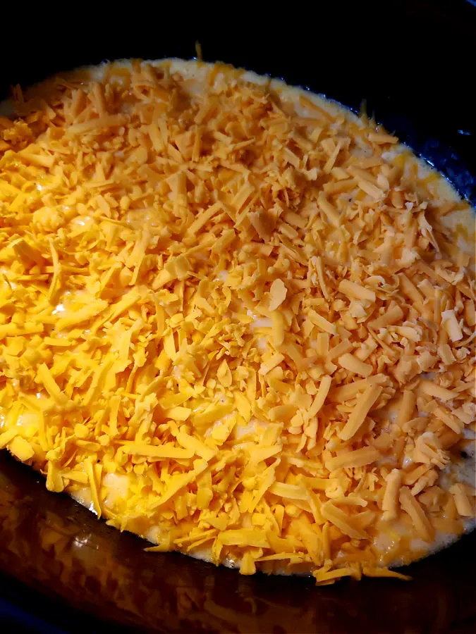 Slow cooker macaroni mixture topped with shredded cheese before slow cooking
