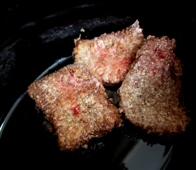 partially cooked browned cube steaks in a crockery of the slow cooker