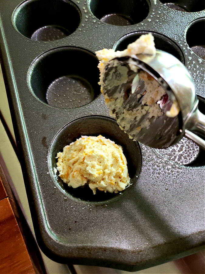 Adding sour cream biscuit dough to a muffin tin using a cookie scoop