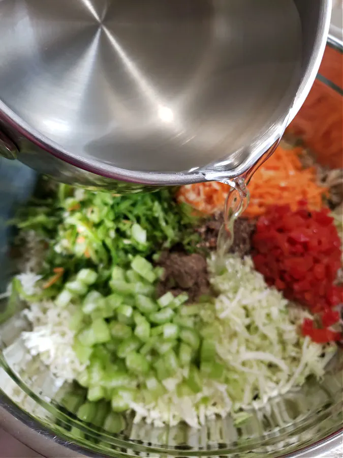 Vinegar-Based Dressing being poured over coleslaw vegetables