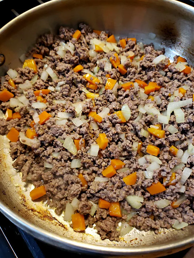 Ground beef with bell pepper and onion cooking in a stainless skillet
