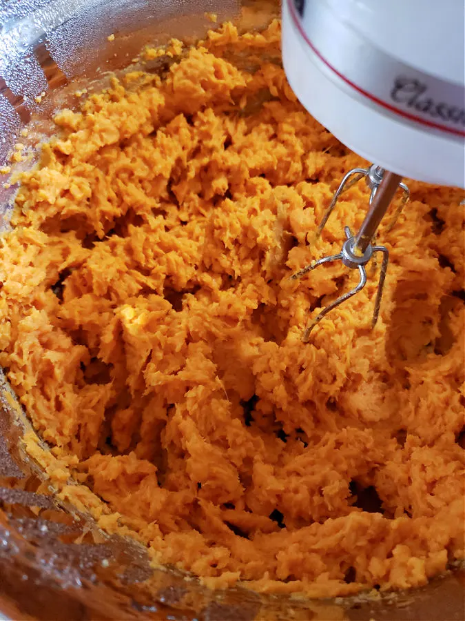 using a hand mixer to whip sweet potatoes in a mixing bowl