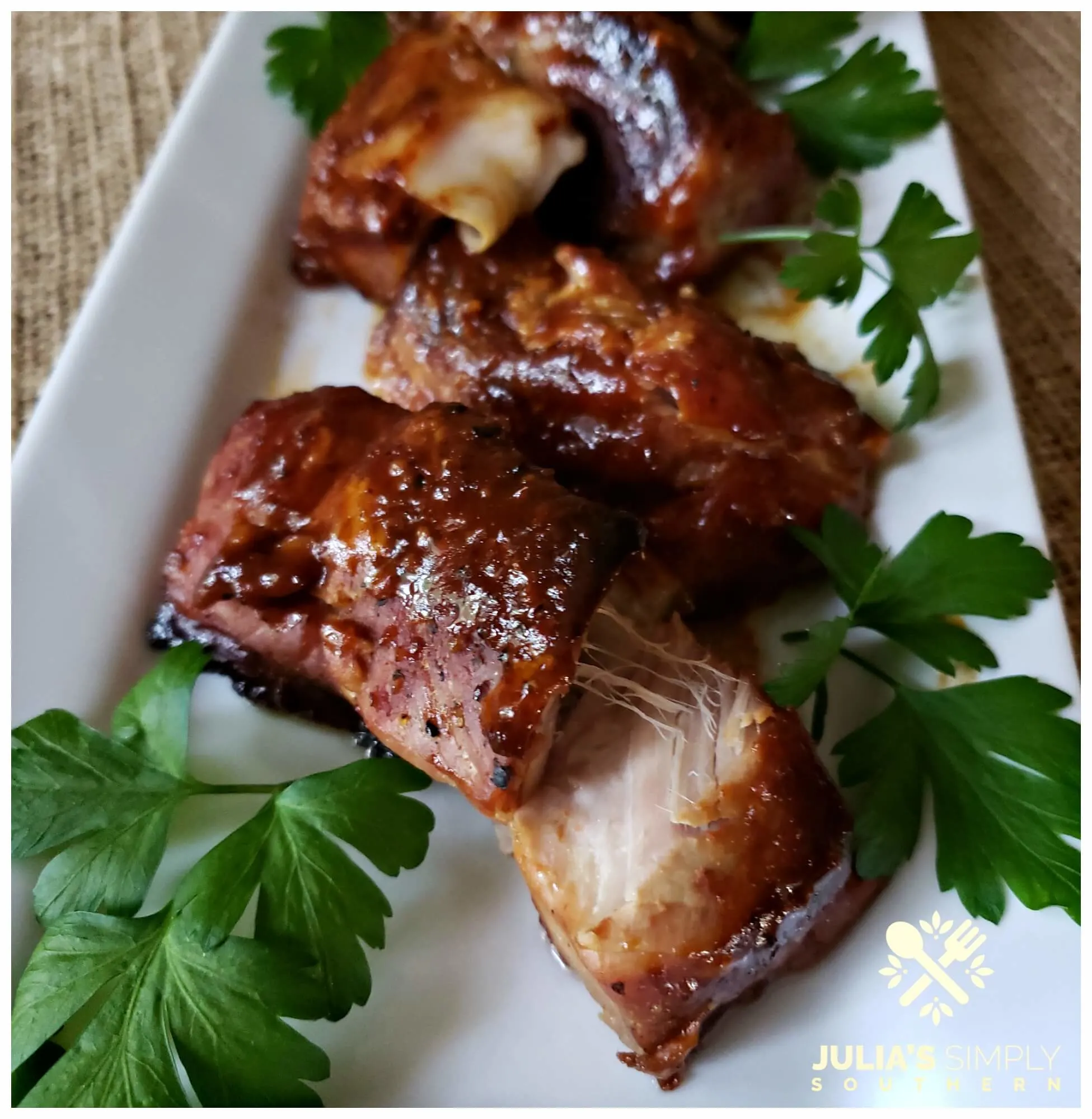 Tender boneless Easy Country-Style Pork Ribs Recipe with BBQ cooked slow in the oven until they are tender and fall apart delicious. Served on a white platter garnished with parsley.