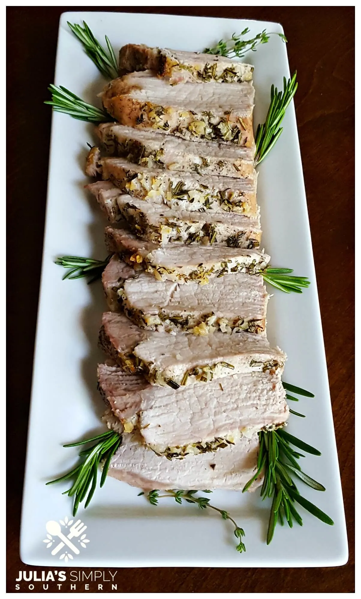 White platter with sliced pork loin roast crusted with herbs and garlic