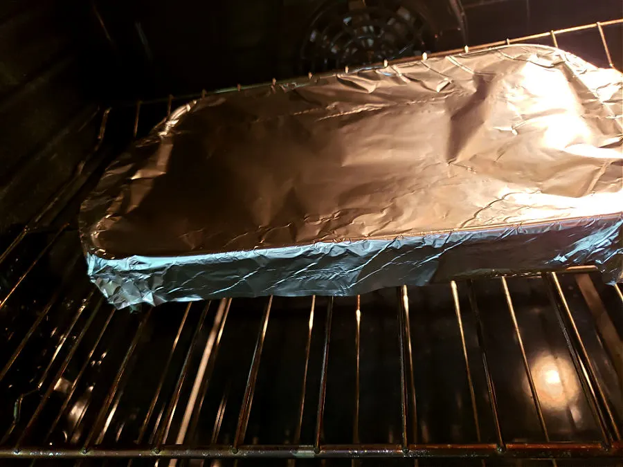 aluminum foil covered baking dish with pork chops and rice casserole in an oven baking