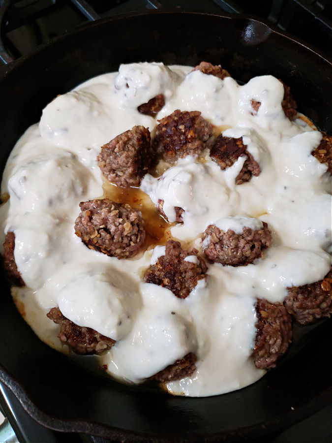 Adding the creamy mushroom sauce mixture to the meatballs in the skillet