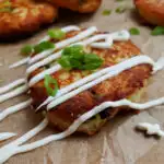 sour cream drizzled over a fried mashed potato cakes patties garnished with scallions