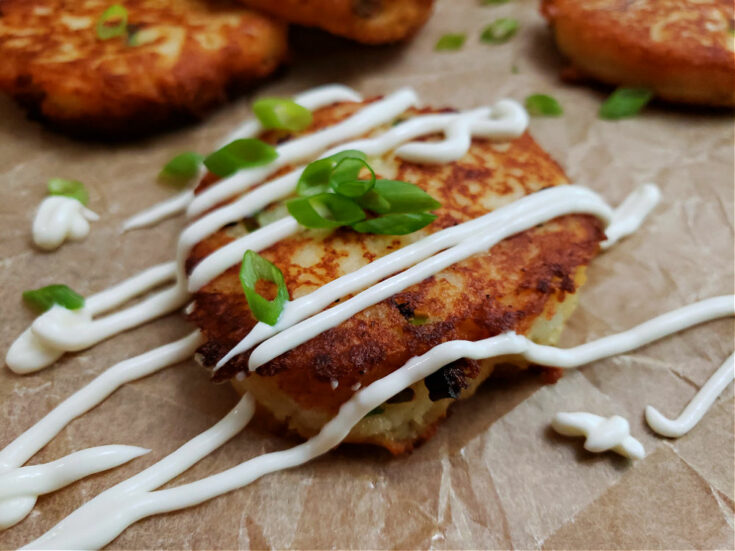 sour cream drizzled over a fried mashed potato cakes patties garnished with scallions