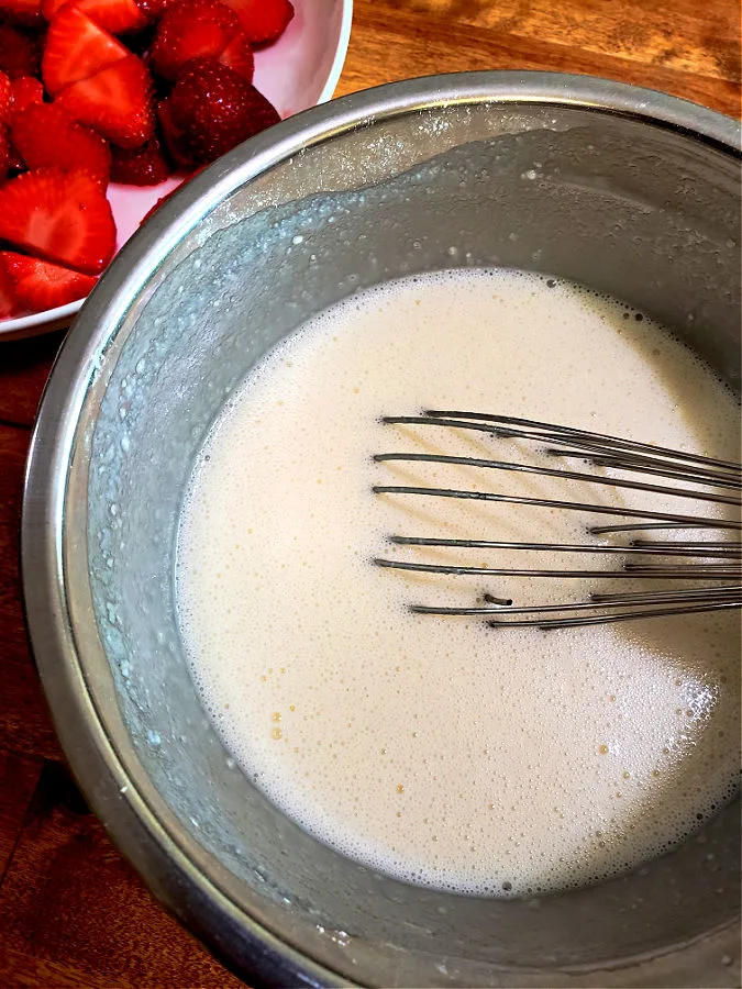 Mixing bowl with whisk combining batter for fruit desserts containing a cup of the white sugar, cup of self rising flour (not all purpose) and cup of milk with vanilla