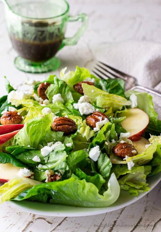 Fall salad with apples and pecans on a plate with a cider dressing to the side 