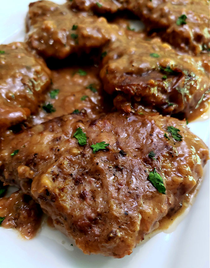 tender cube steaks with brown gravy prepared in the slow cooker served on a white platter and garnished with chopped parsley
