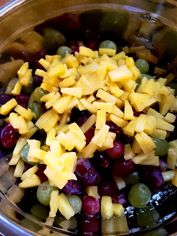 Crisp grapes and pineapple tidbits in a large mixing bowl with cream cheese and sour cream dressing