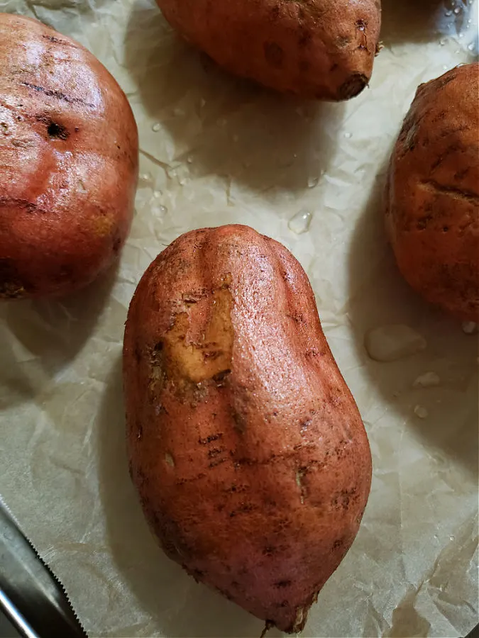 baking sheet lined with parchment and washed sweet potatoes ready for baking